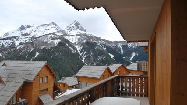 A wooden chalet with a balcony overlooking snow-covered mountains.