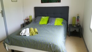 Ein ordentlich bezogenes Bett mit einer grau-grünen Tagesdecke, zwei Kissen mit grünen und grauen Akzenten und zwei gerollte Handtücher in Weiß und Grün.