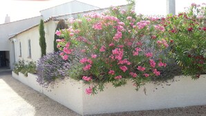 Ein Gebäude mit weißer Fassade, einem Steinkamin und einem Garten mit rosa Blumen und Lavendel.