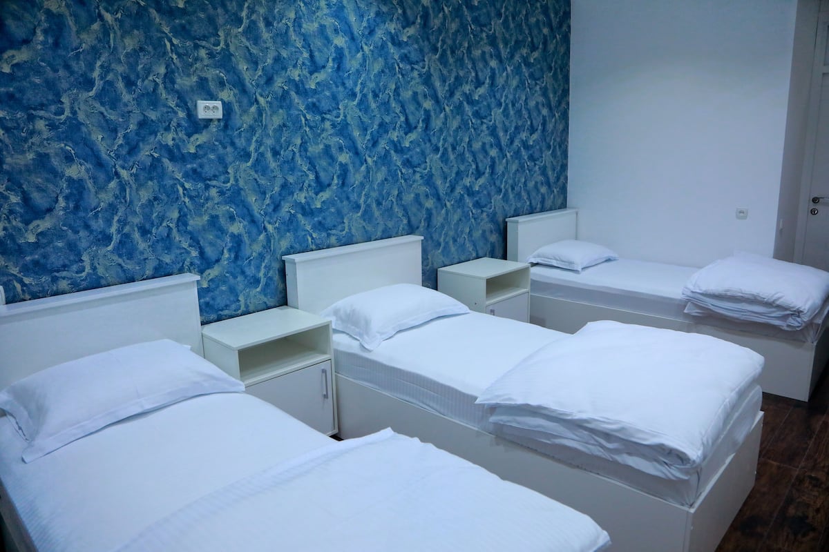 Ein Hotelzimmer mit drei Einzelbetten, weißen Kopfteilen und einer blauen Wand mit Struktur.