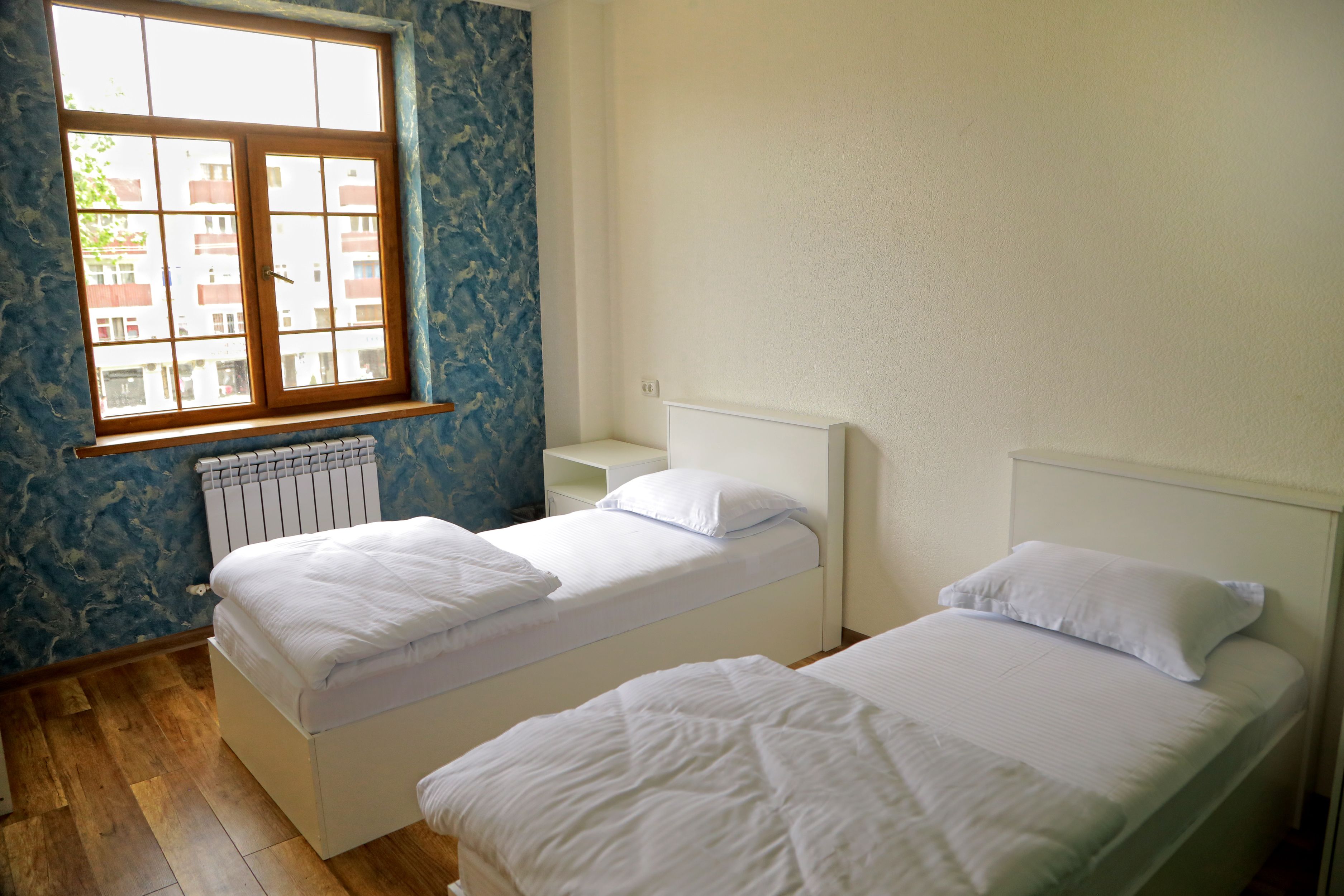 A room with two single beds, a window with a view of buildings, and a radiator.