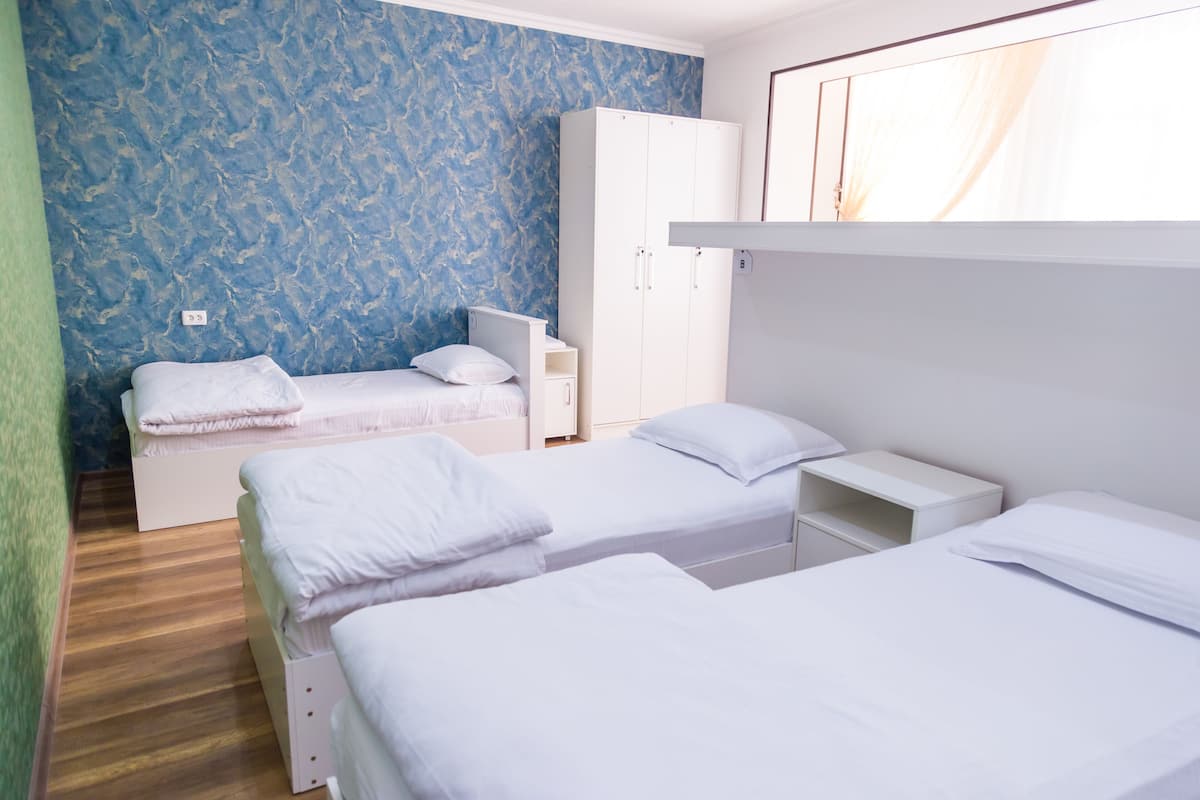 Ein Zimmer mit zwei Einzelbetten, einem Kleiderschrank, einem Nachttisch und einer Wand mit blauem Muster.