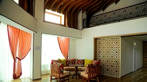A spacious living room with a high ceiling, wooden flooring, a round coffee table, and a sofa with colorful cushions. - MANIJA Hostel (Samarkand)
