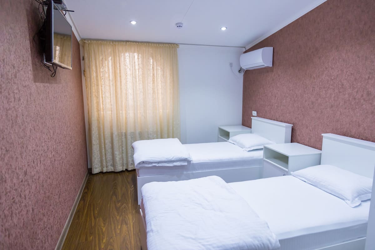 Ein Hotelzimmer mit zwei Einzelbetten, einem an der Wand montierten Fernseher und einer Klimaanlage.