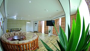 A living room with a round wooden sofa, a small table, and a TV mounted on the wall. - MANIJA Hostel (Samarkand)