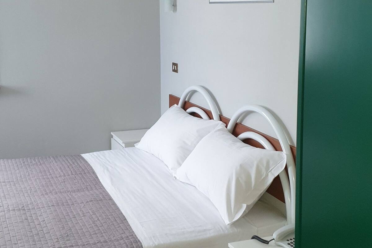 A neatly arranged bedroom with a bed, bedside tables, and a wall-mounted light fixture.