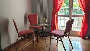 A room with a wooden floor, a table with two chairs, a framed picture on the wall, and a window with red curtains. - Nuovo Hotel Sporting (Campagnola Emilia)