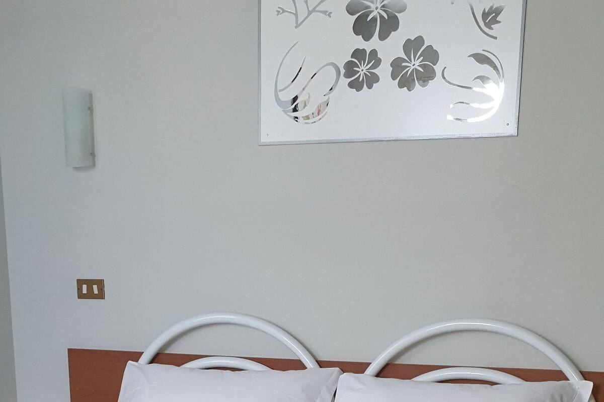 A bed with white metal headboard and footboard, a white mattress, and a grey blanket.