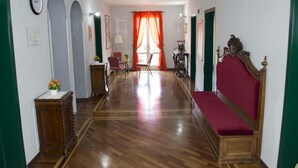 A hallway with a wooden floor, a bench, a table with a vase of flowers, and a chair. - Nuovo Hotel Sporting (Campagnola Emilia)