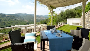 Eine Terrassensitzgelegenheit im Freien mit einem für Tee gedeckten Tisch, umgeben von Korbstühlen, mit Blick auf ein üppiges Tal.