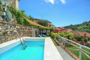A swimming pool with a stone wall, a ladder, and a shaded area.
