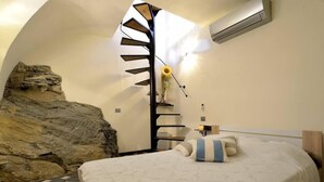 Ein Schlafzimmer mit einem Bett, einer einzigartigen Spiraltreppe, einer Felswand und einem kleinen Tisch mit einer Vase voller Sonnenblumen.