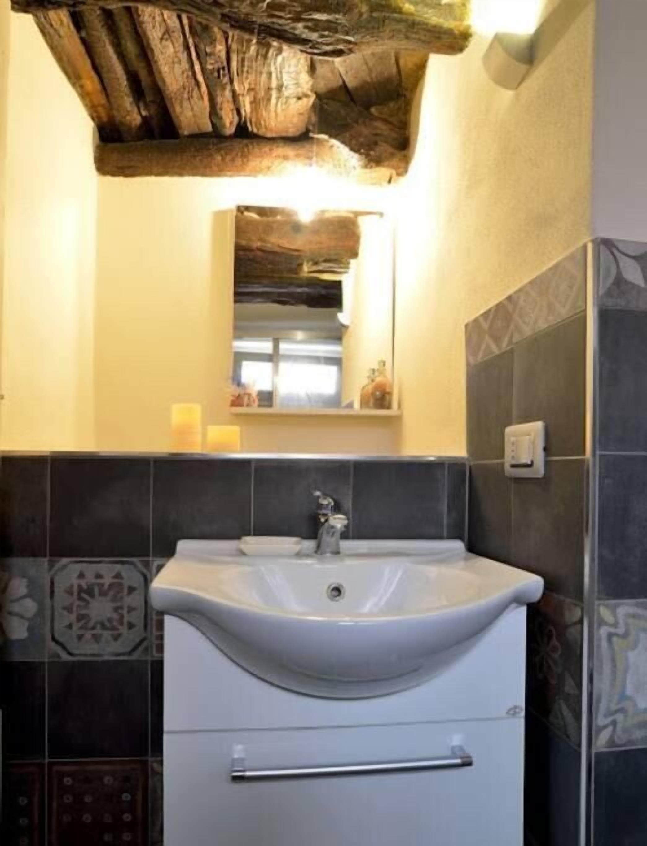 Une salle de bain avec un lavabo blanc, un miroir au-dessus, et des carreaux de couleur foncée à motifs sur les murs.