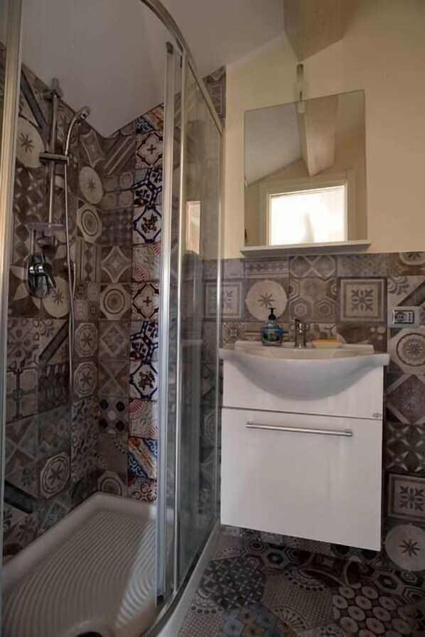 A bathroom with patterned tiles, a glass shower enclosure, a white sink with a mirror, and a small window.