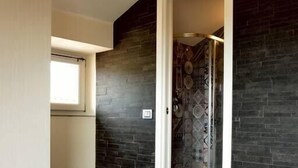 Ein modernes Badezimmer mit dunkel gefliesten Wänden, einer Dusche mit einem gemusterten Fliesendesign und einem Fenster, das natürliches Licht hereinlässt.