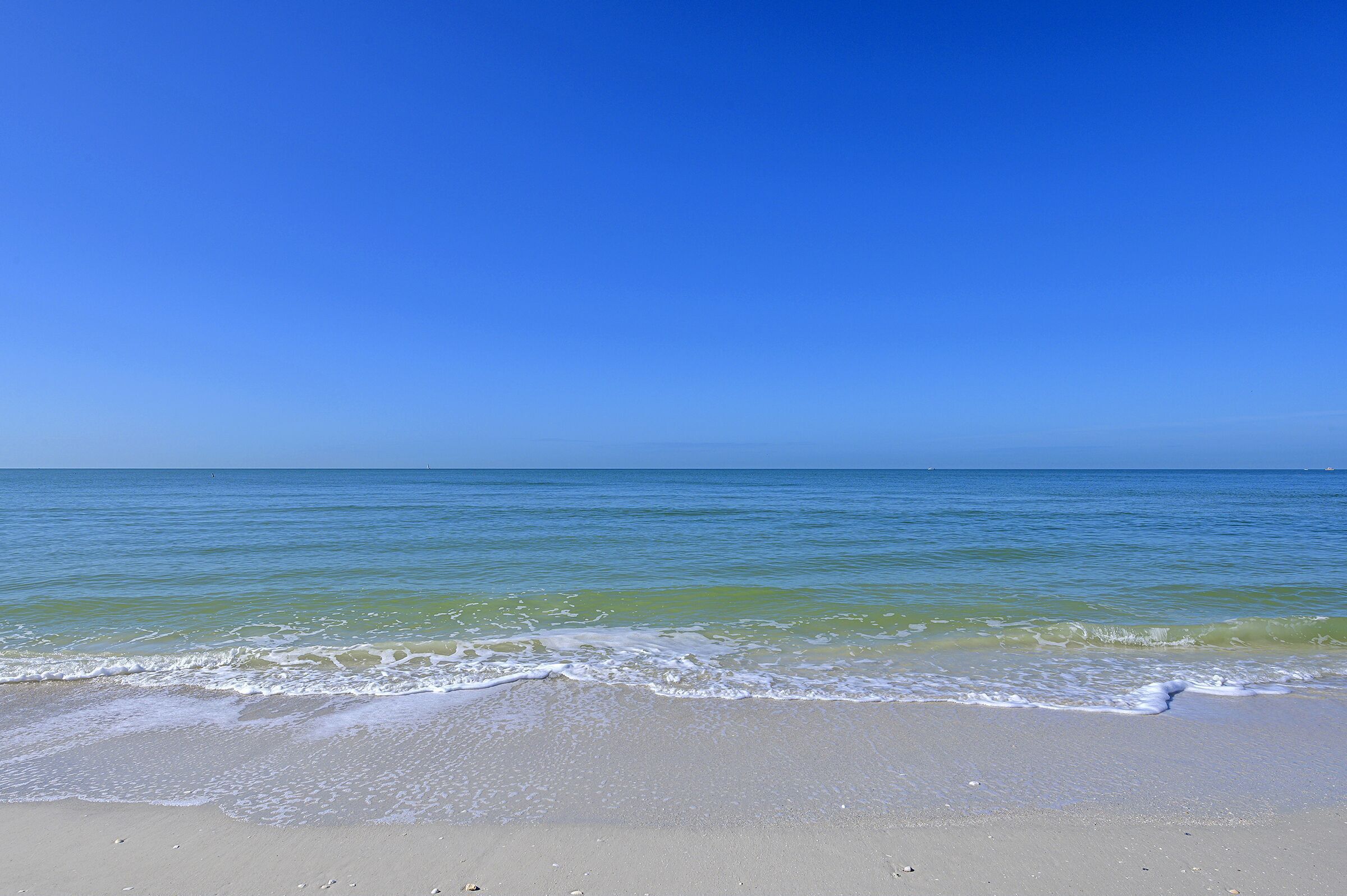 A beach with clear blue water and a sandy shore.