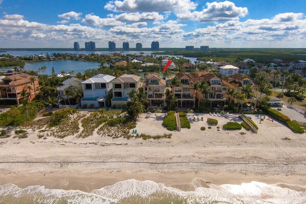 Un quartier résidentiel situé sur la côte, avec des propriétés donnant sur la plage, une plage de sable et une vue lointaine sur les gratte-ciel de la ville.