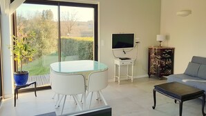Un soggiorno moderno con un tavolo in vetro, due sedie bianche, un divano grigio, una televisione e un mobile contenitore con opere d'arte.