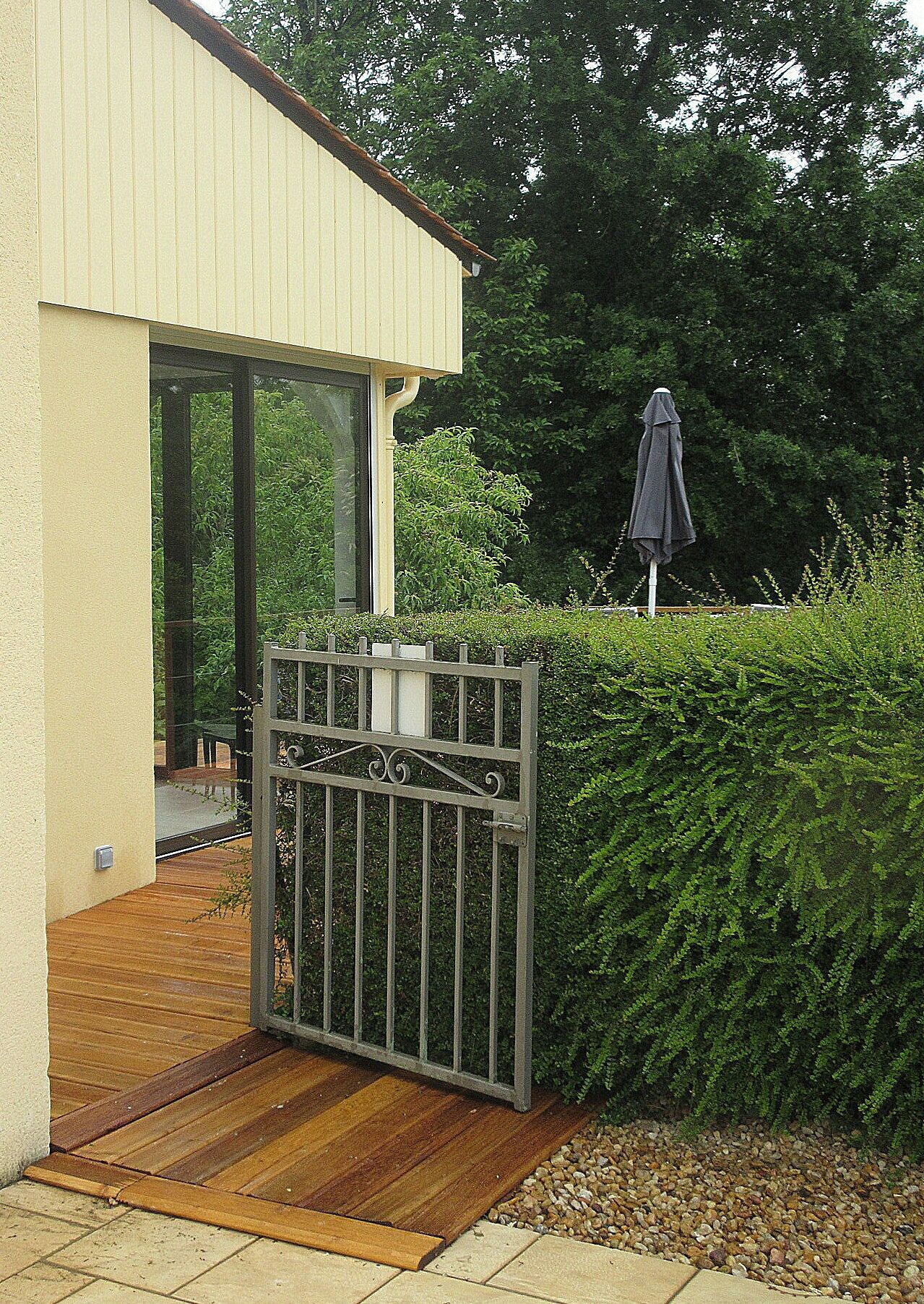 Un ingresso recintato a un edificio con una terrazza in legno e un cancello in metallo.