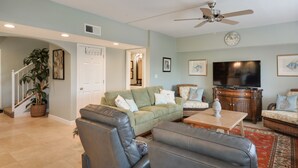 A spacious living room with a green sofa, a leather armchair, a wooden coffee table, and a television.