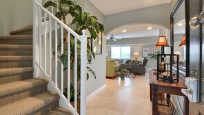 A staircase with beige carpeted steps and white railings, leading to a living area with a sofa, armchairs, and a coffee table.