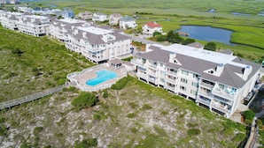 A residential complex with multiple two-story buildings, a central swimming pool, and a surrounding natural landscape. - Oceanfront Condo with Ocean Views (Wrightsville Beach)
