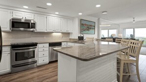 A modern kitchen with white cabinetry, stainless steel appliances, and a large island with a marble countertop. - Oceanfront Condo with Ocean Views (Wrightsville Beach)