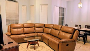 A living room with a brown leather sectional sofa, a glass coffee table, a dining table with chairs, and a television on a wooden stand. - Your next magical getaway! Spacious 3 bedroom, 2 bath condo in gated community. (Davenport)