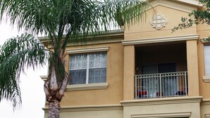 A multi-story building with balconies, large windows, and a palm tree in front. - Your next magical getaway! Spacious 3 bedroom, 2 bath condo in gated community. (Davenport)
