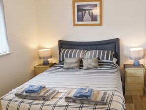 A neatly made bed with striped bedding, two bedside lamps, a wooden nightstand, and a framed picture on the wall.