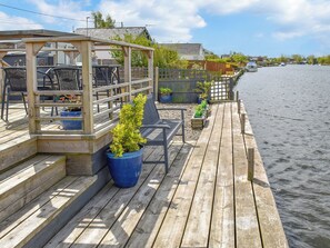 Terraza de madera con mobiliario exterior, plantas en macetas y vista al agua.