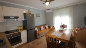 Eine kleine Küche mit Kühlschrank, Herd und Backofen. Ein Esstisch mit Stühlen und ein Deckenventilator sind vorhanden.