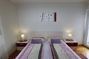 Una habitación de hotel con dos camas, mesitas de noche con lámparas, una obra de arte en la pared y una ventana.