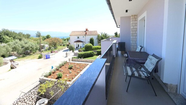 Ein Balkon mit Tisch und Stühlen, Blick auf einen Garten und ein Gebäude im Hintergrund.