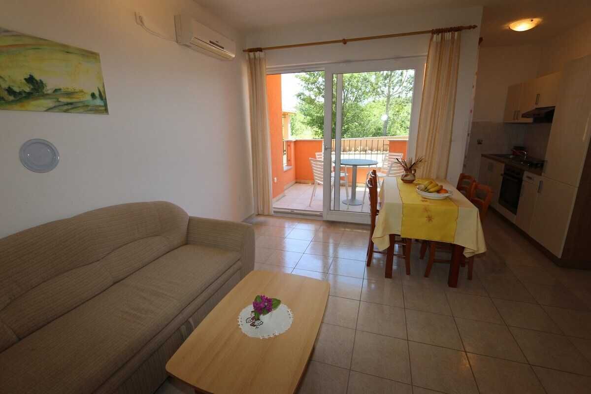 Un soggiorno con divano, tavolino da caffè con un fiore, zona pranzo con tavolo e sedie, e una porta vetrata scorrevole che dà su un'area esterna.