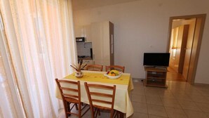 A dining area with a table set for two, a television, and a kitchen in the background. - Apartment Dudovic Damir A2 nr 1 (Silo - island Krk)