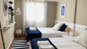 Ein Hotelzimmer mit zwei Betten, einem Streifenmuster-Teppich, einer Hängelampe und einem an der Wand befestigten Kunstwerk.