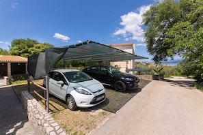 Zwei Autos stehen unter einer Überdachung mit einer Steinwand und einem Gebäude im Hintergrund.