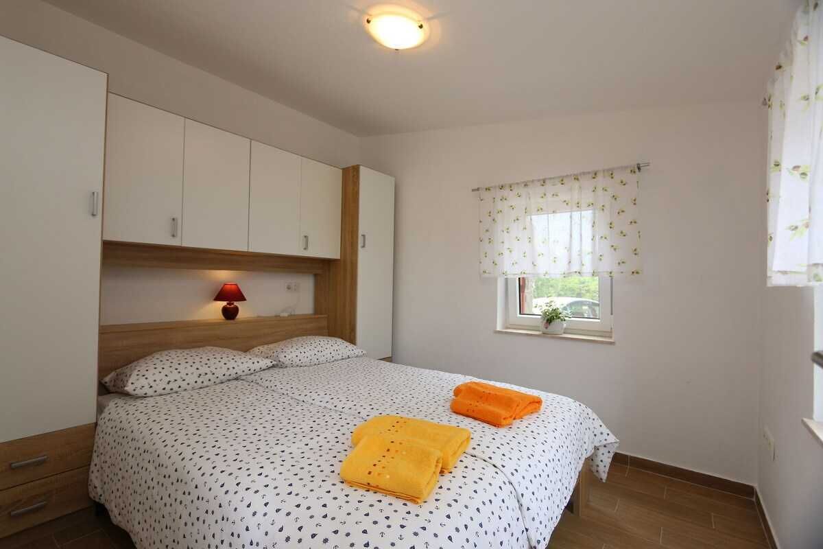 Ein Schlafzimmer mit Bett, Nachttisch, Fenster mit Vorhängen und Deckenleuchte.