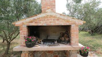 Un horno de ladrillo al aire libre con una chimenea, rodeado de árboles.