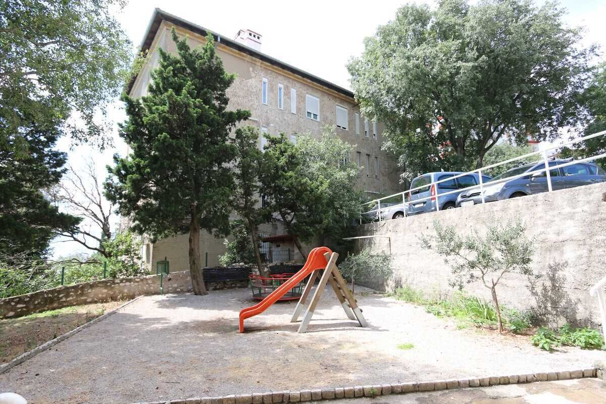 Un parque infantil con un tobogán, rodeado de árboles y un edificio.