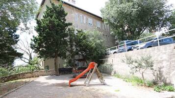 Un parque infantil con un tobogán, rodeado de árboles y un edificio.
