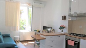 A compact living space with a kitchenette, a sofa, a small table, and a window with curtains. - Krimeja apartment close to Pecine beach and center (Rijeka)