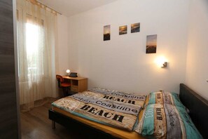 A bedroom with a bed, a desk, and a chair. There are three wall-mounted pictures and a wall-mounted light.