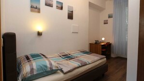 A bedroom with a bed, a desk, and a chair. There are wall-mounted lights and a window with curtains. - Krimeja apartment close to Pecine beach and center (Rijeka)