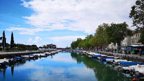 A calm river with boats docked on both sides, surrounded by trees and buildings. - Krimeja apartment close to Pecine beach and center (Rijeka)