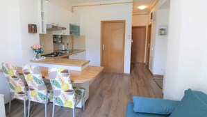 A compact living space with a kitchenette, a dining area with patterned chairs, and a blue sofa. - Krimeja apartment close to Pecine beach and center (Rijeka)
