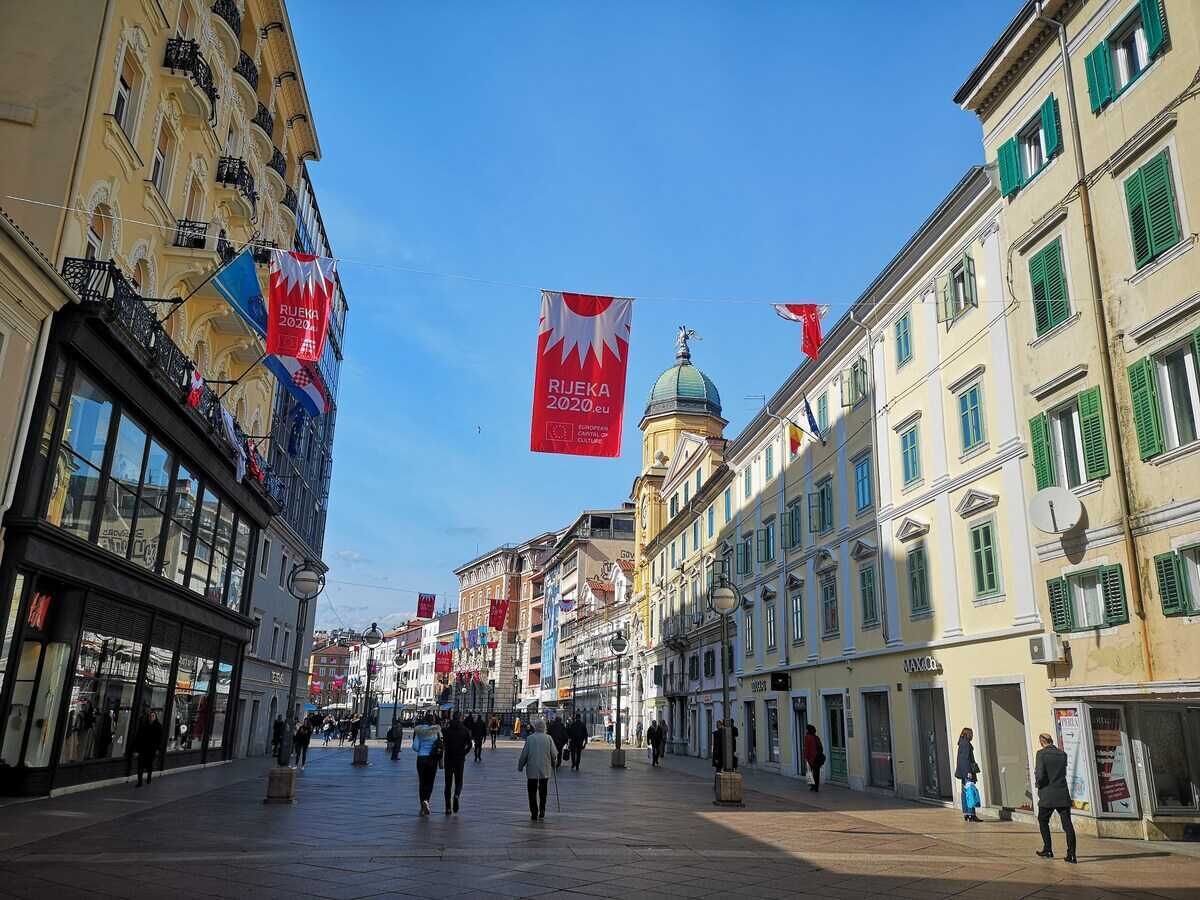 Ancha calle peatonal con edificios históricos, banderas y cielo despejado.