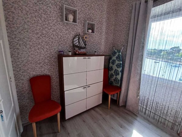 Una habitación con piso de madera, un armario blanco, dos sillas rojas, una ventana con vistas y una cortina estampada.