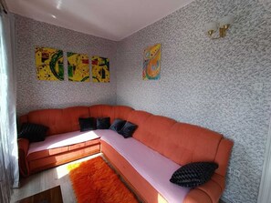 A room with a curved orange sofa, a pink bench, and a red rug. There are three abstract paintings on the wall.